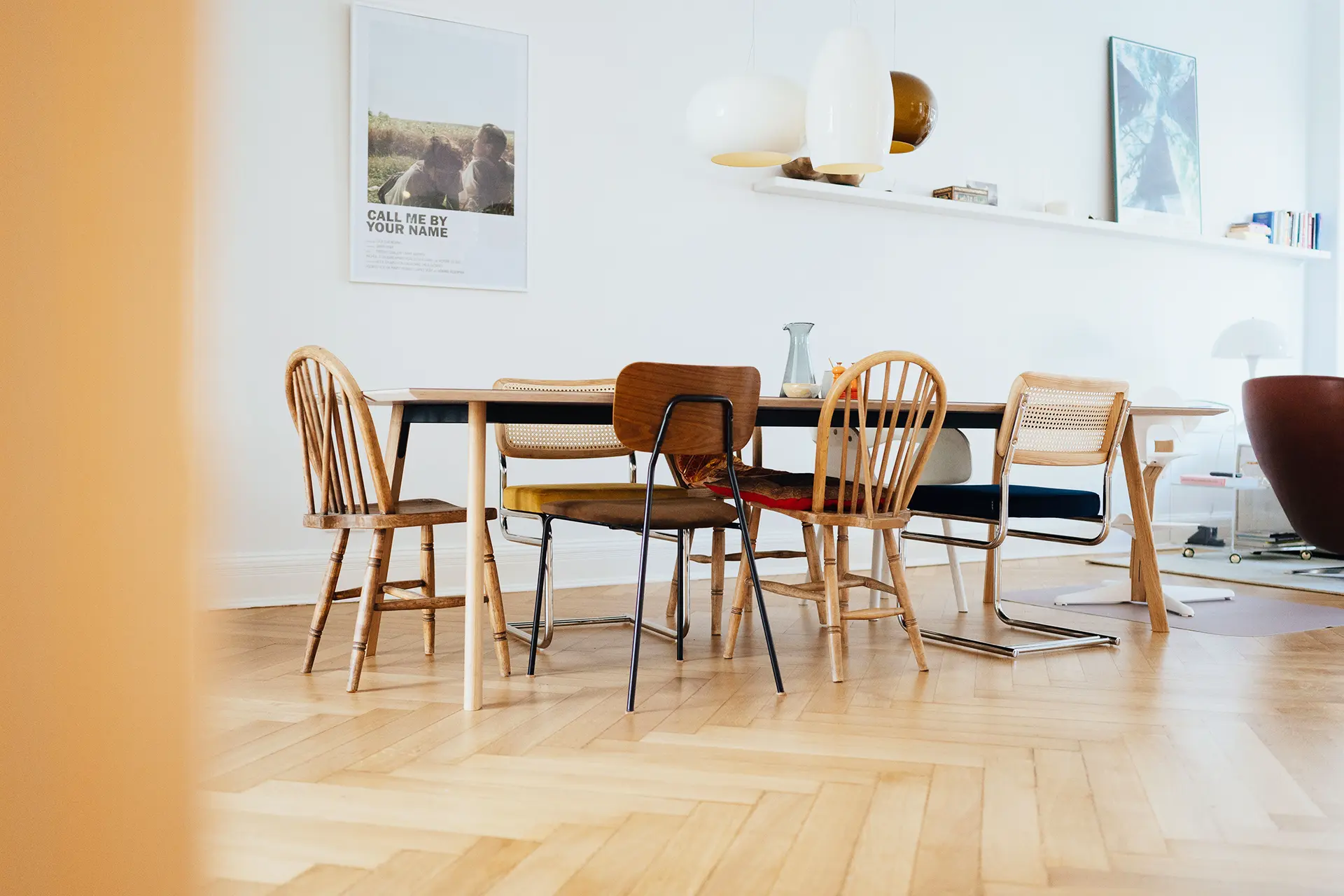In einem mit Tageslicht durchfluteten Esszimmer steht ein Holztisch. Darum sind acht verschiedene Stühle angeordnet.
